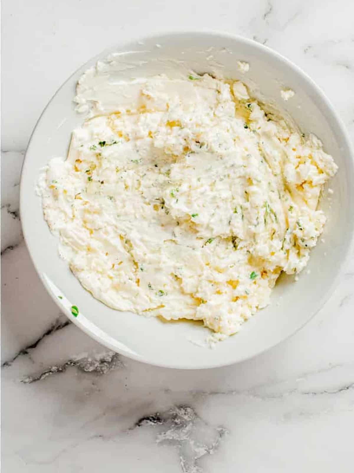 Goat cheese, cream cheese, scallions, and parsley mixed smooth in a white bowl.