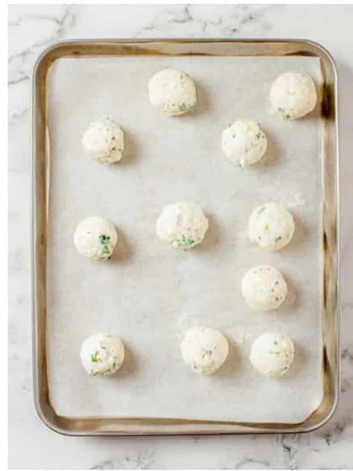 Mini goat cheese balls rolled and arranged on a parchment lined sheet tray.