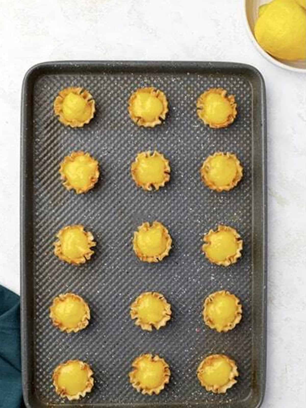 Mini phyllo shells filled with lemon curd on a baking sheet.