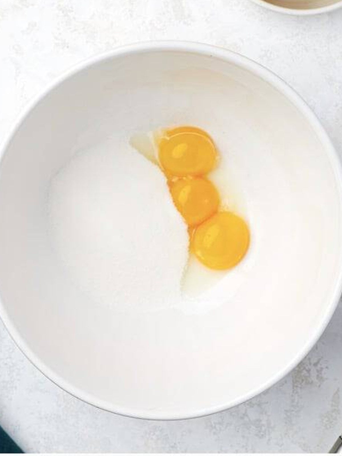 Egg yolks and sugar in a white bowl before whisking for the lemon curd.