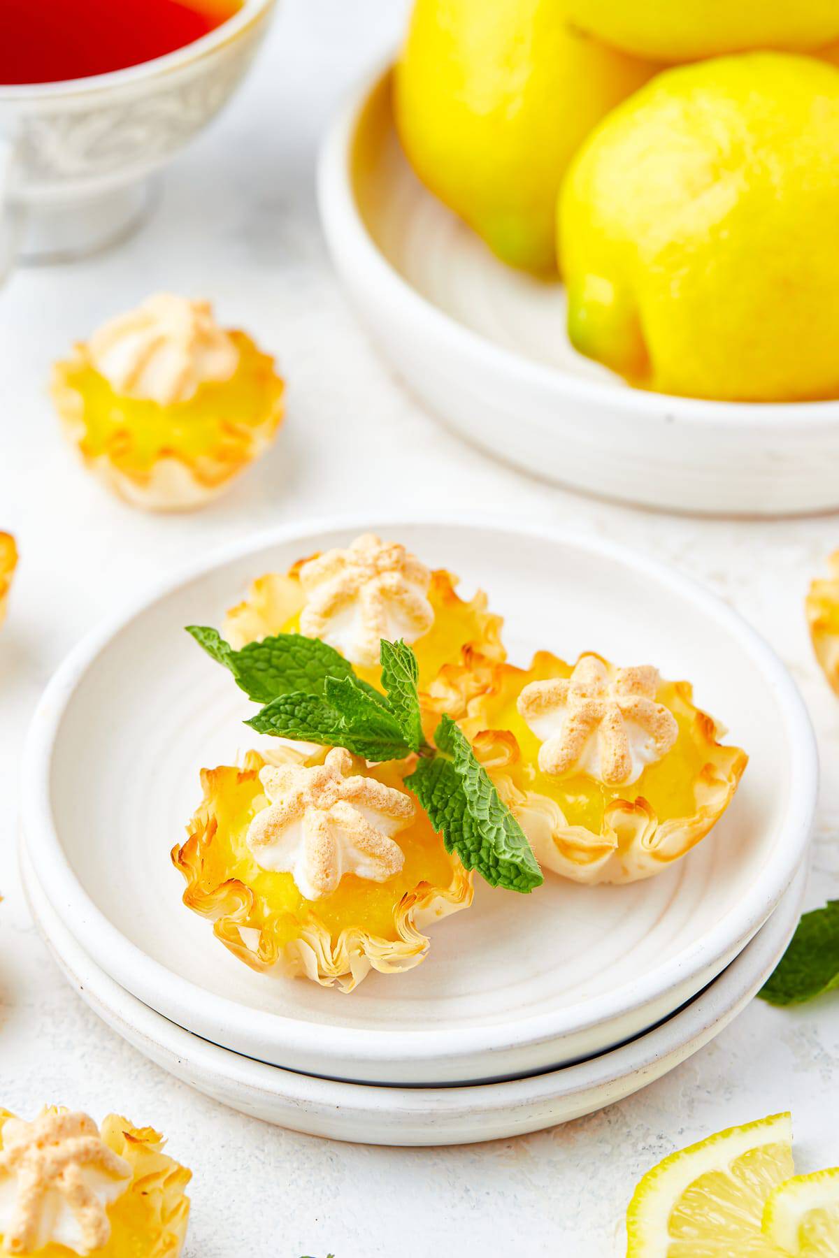 Mini lemon meringue pies on a white plate garnished with fresh mint and lemon slices.