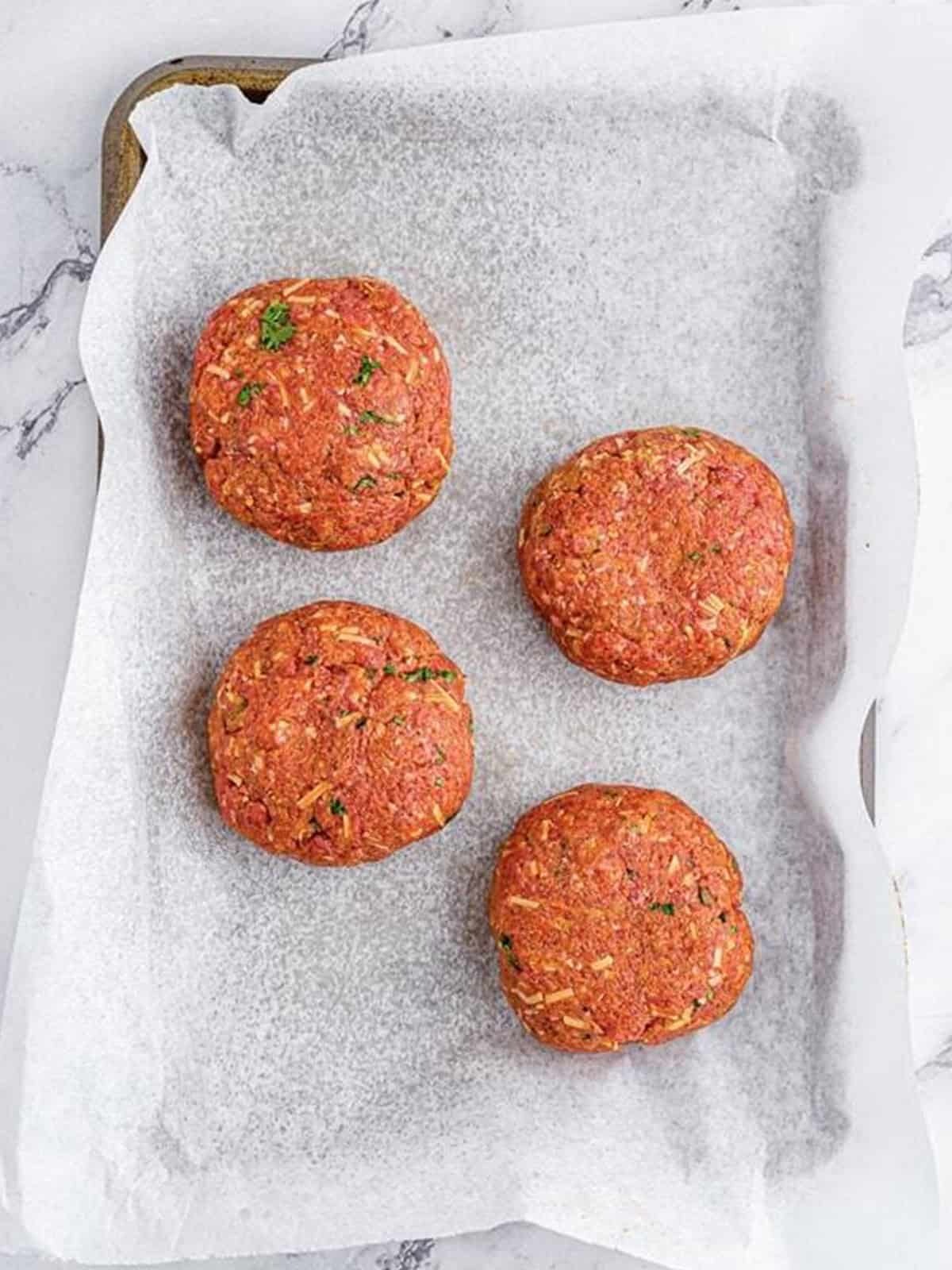 Four formed mini meatloaf loaves on a parchment lined sheet pan.
