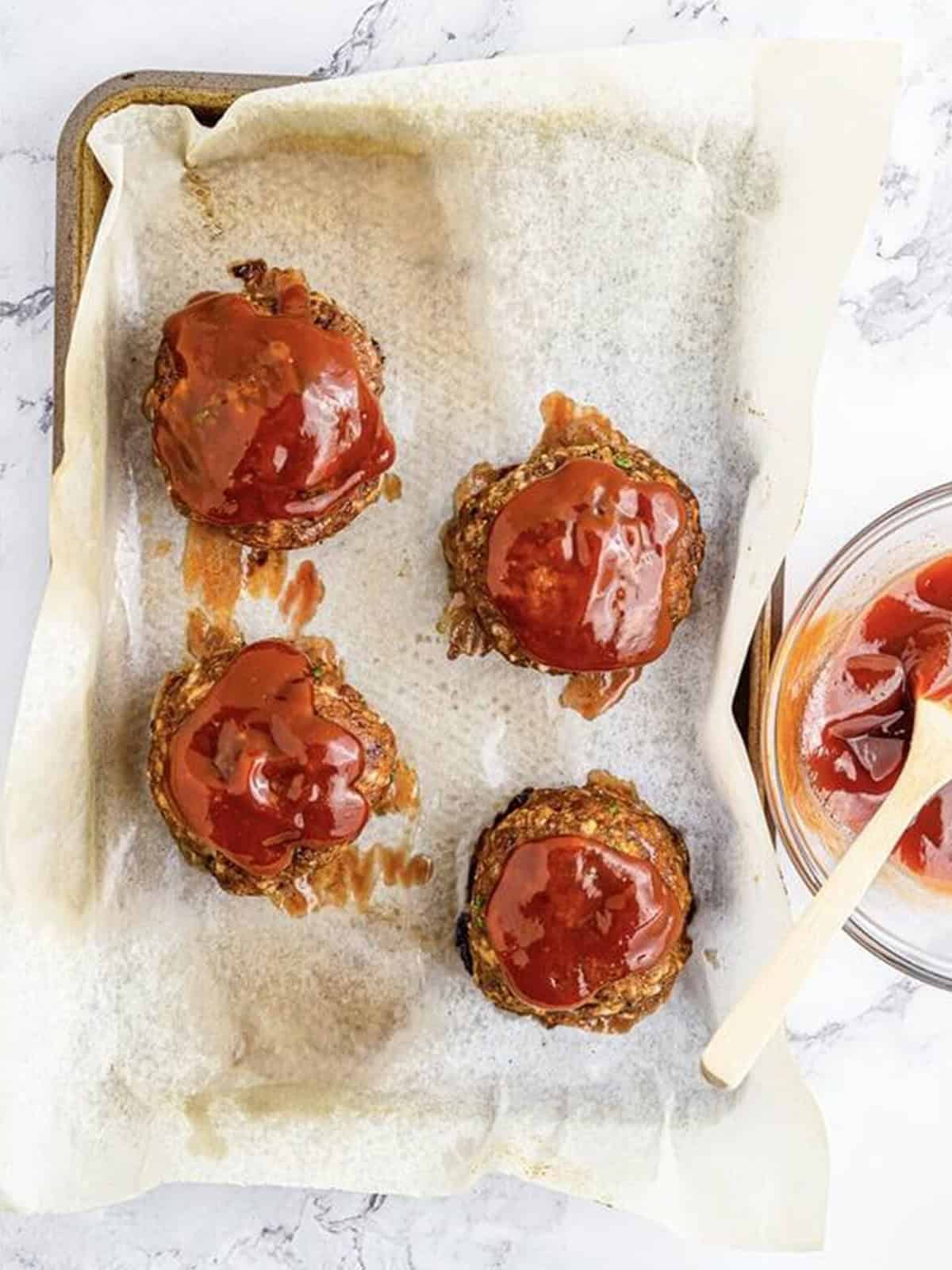 Baked mini meatloaves brushed with glaze on a sheet pan.