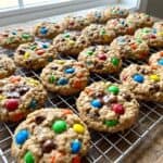 Mini monster cookies on a wire cooling rack studded with colorful candy pieces.