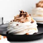 A mini pavlova topped with Nutella whipped cream and chopped hazelnuts on a black plate.