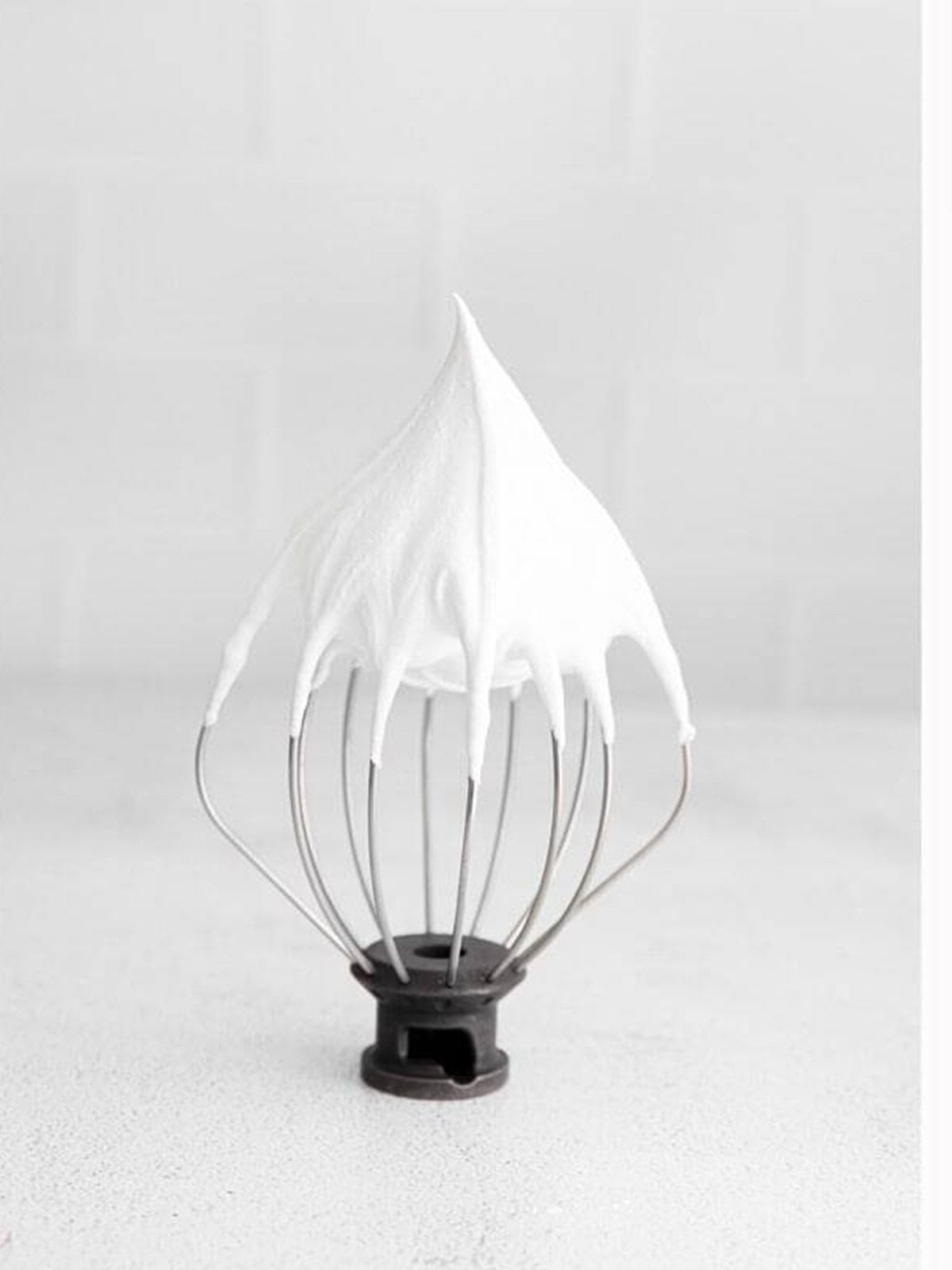Glossy meringue whipped to stiff peaks on a whisk attachment.
