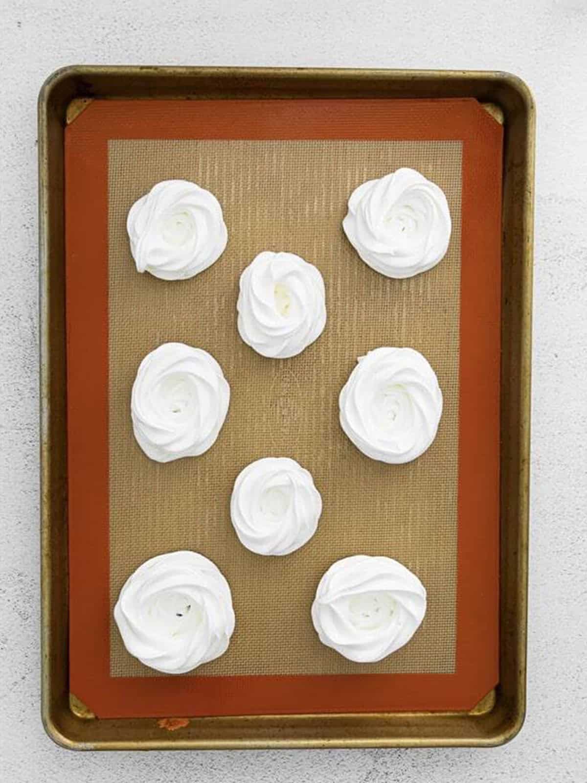 Meringue piped into four-inch circles on a parchment-lined baking sheet.