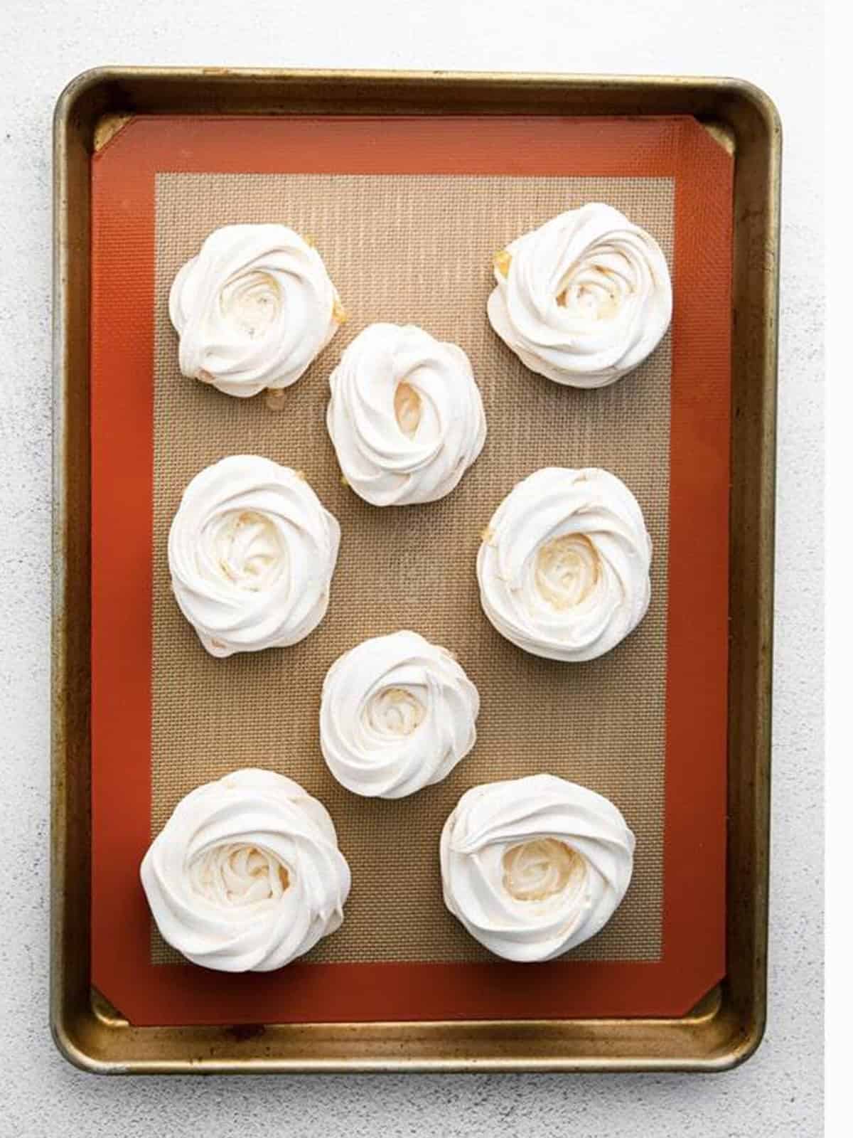 Baked mini pavlova shells cooling on a baking sheet.