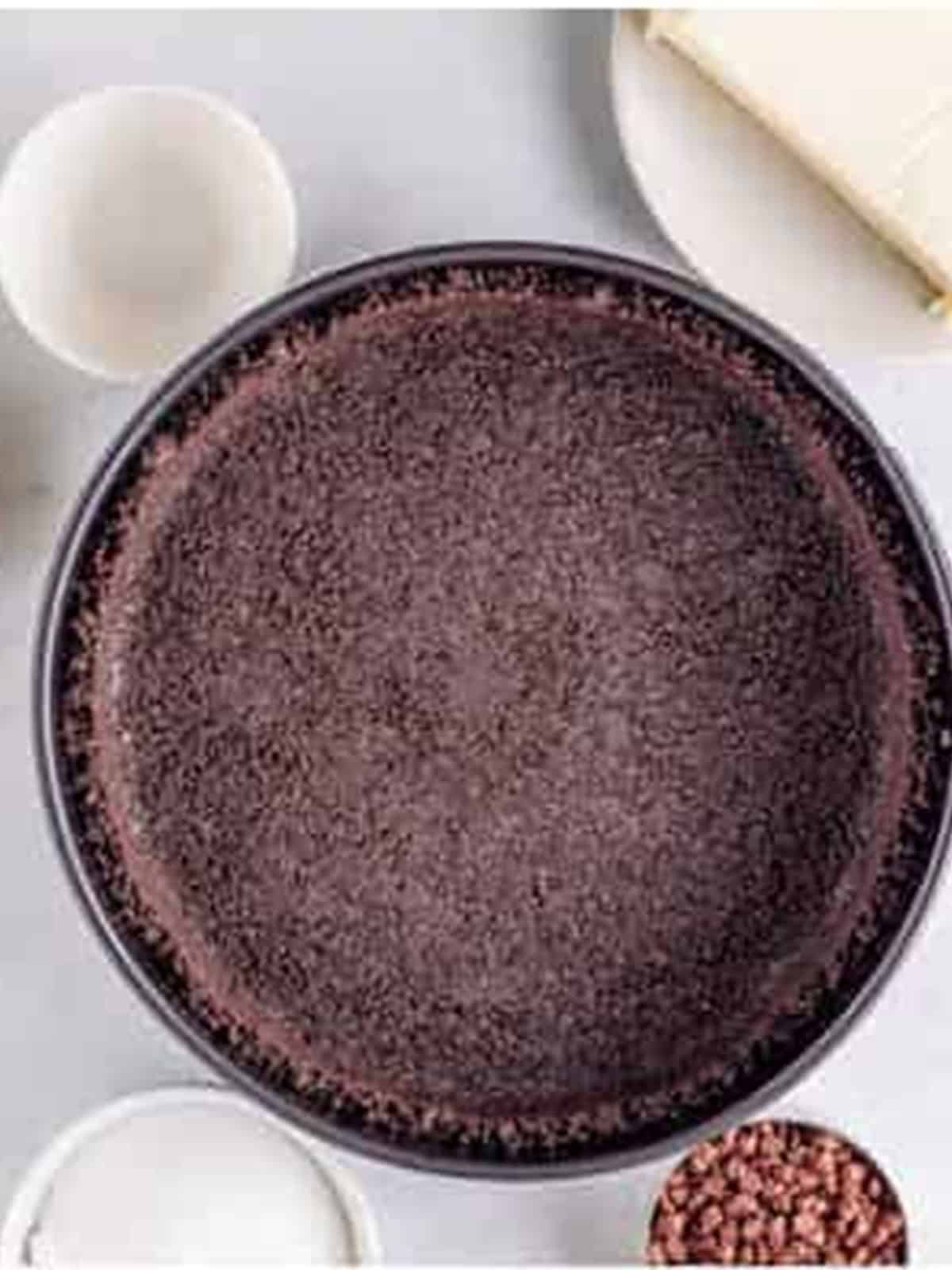 Oreo cookie crust pressed into a springform pan for no bake mint chocolate cheesecake.