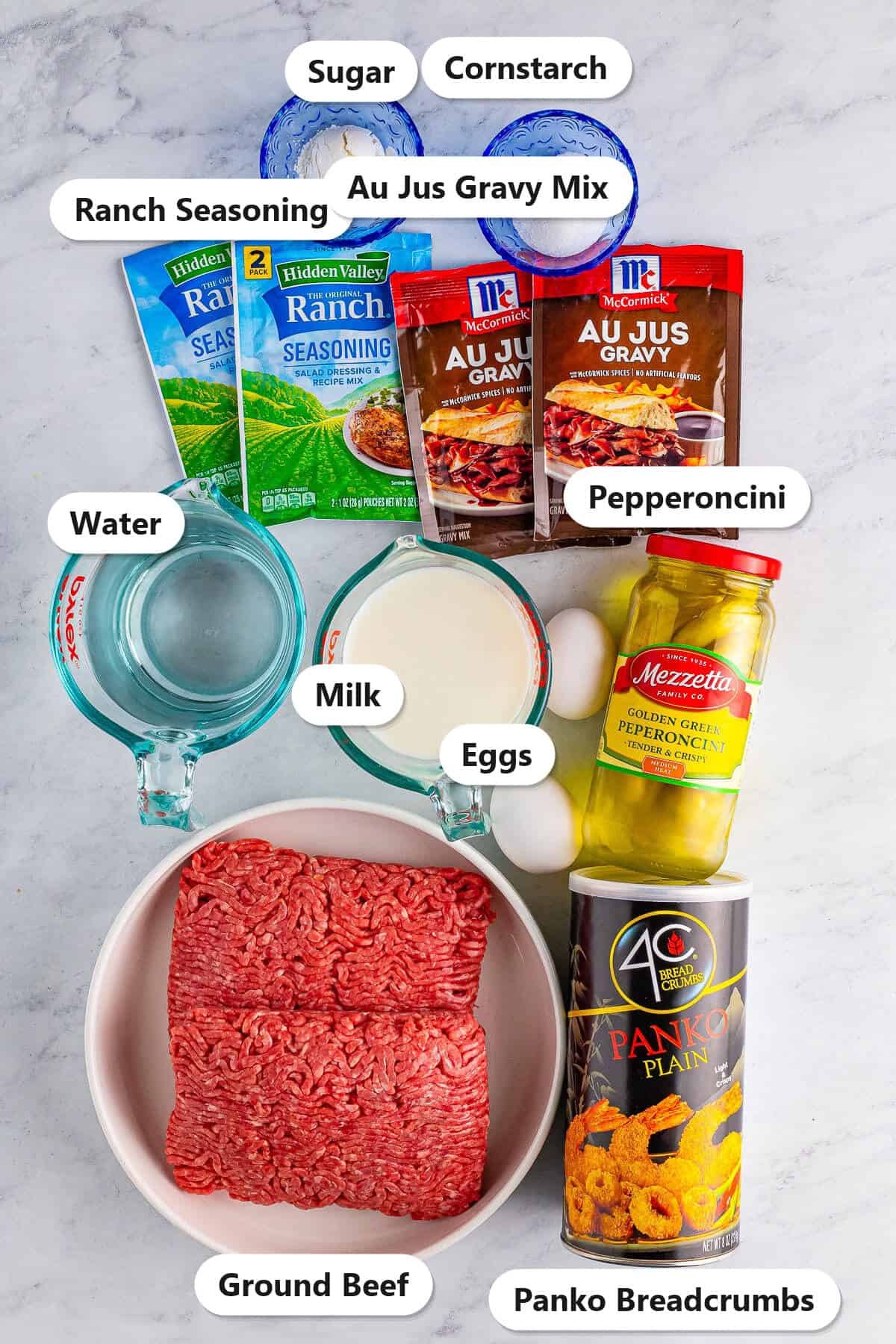 Labeled ingredients for Mississippi crockpot meatloaf including ground beef, ranch seasoning, au jus gravy mix, pepperoncini, panko breadcrumbs, milk, eggs, sugar, cornstarch, and water.