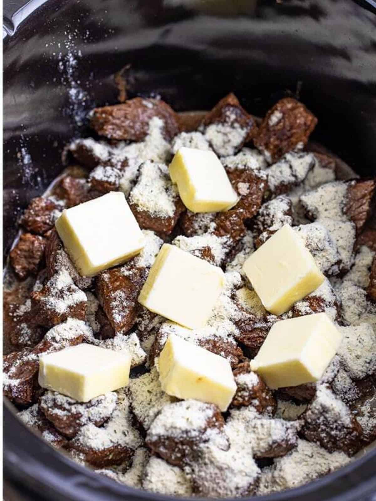 Cubes of butter laid over the seasoned steak bites in the slow cooker.