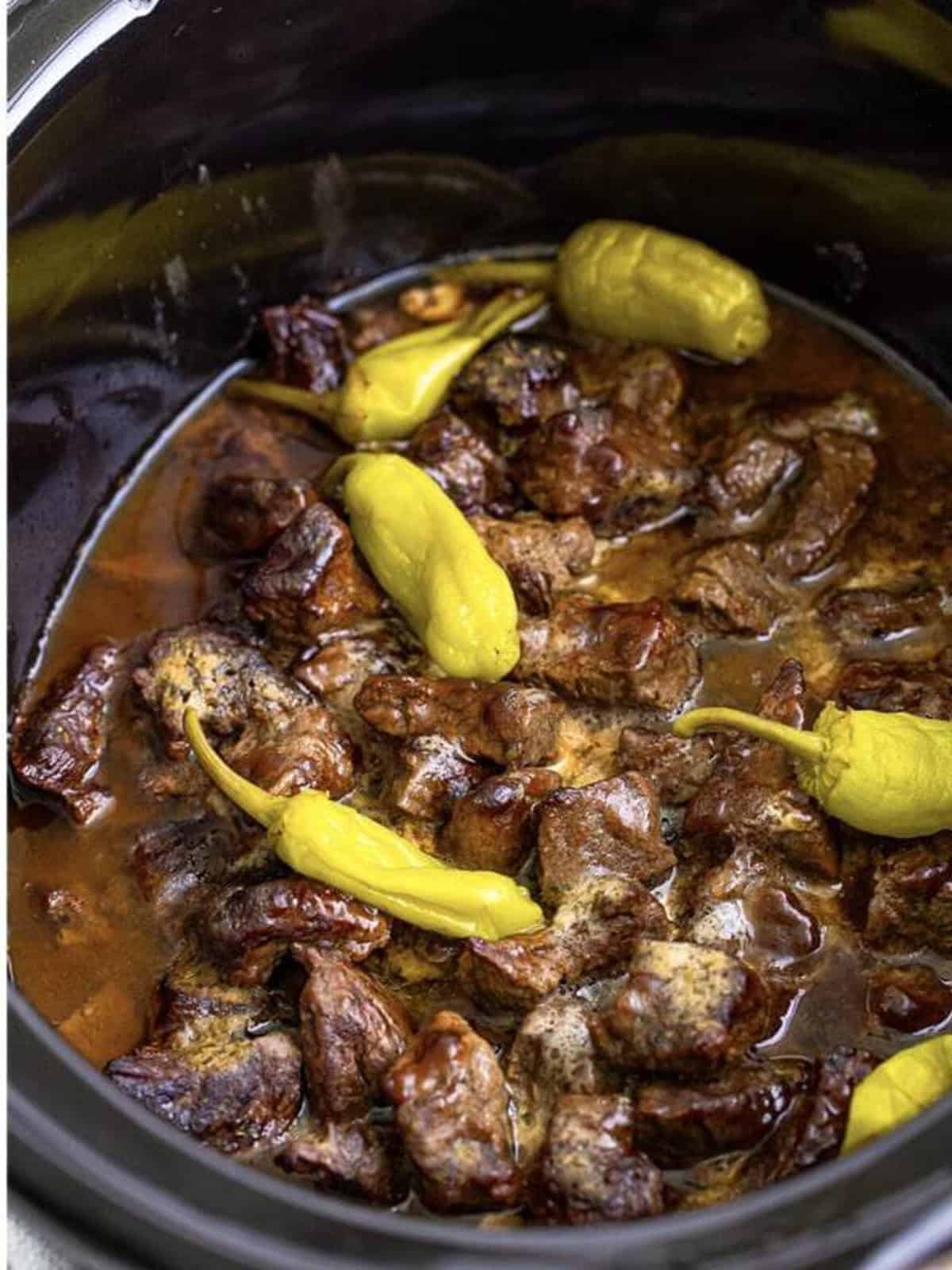 Finished tender Mississippi steak bites in a buttery sauce with pepperoncini in the slow cooker.