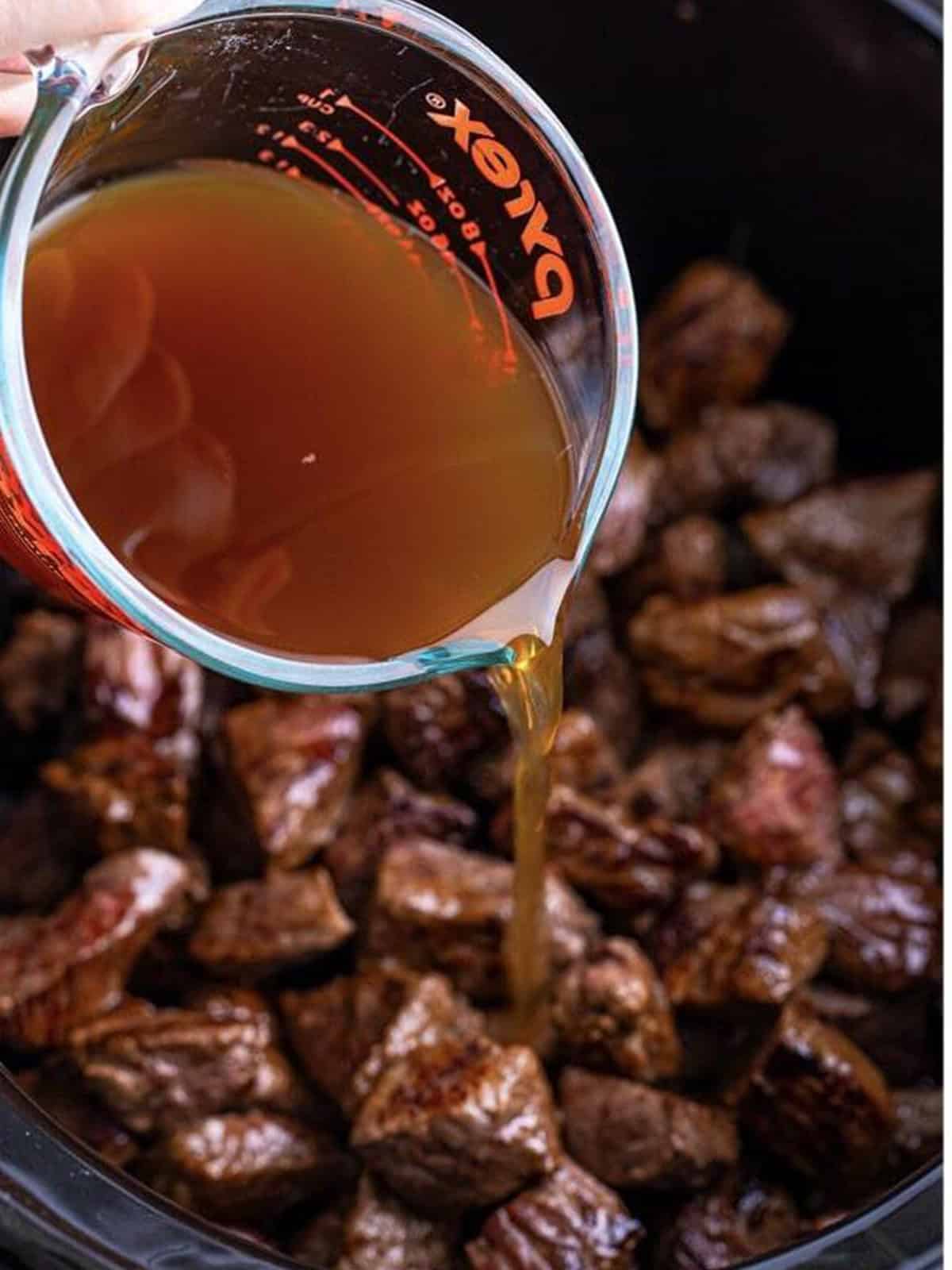 Beef stock poured over the seared steak bites in the slow cooker.