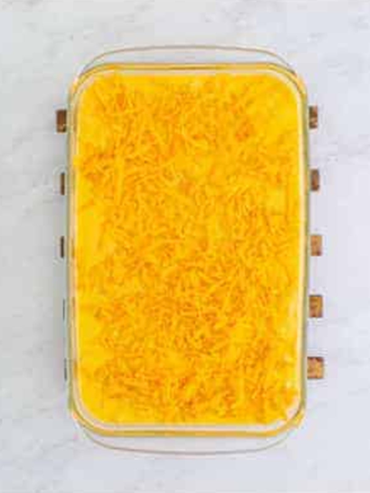 Mac and cheese spread in a baking dish topped with shredded cheddar.