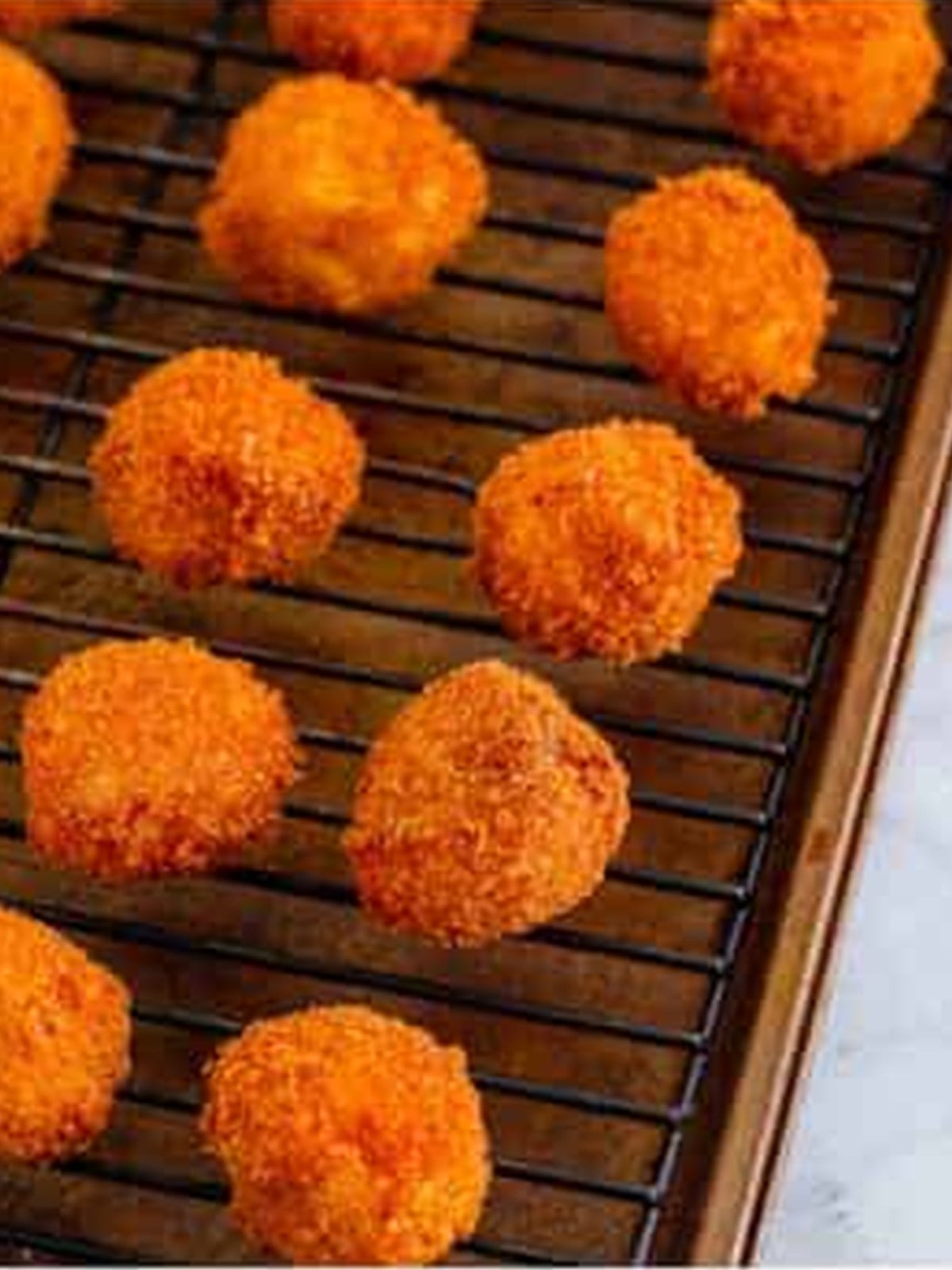 Golden fried mac and cheese balls draining on a wire rack.