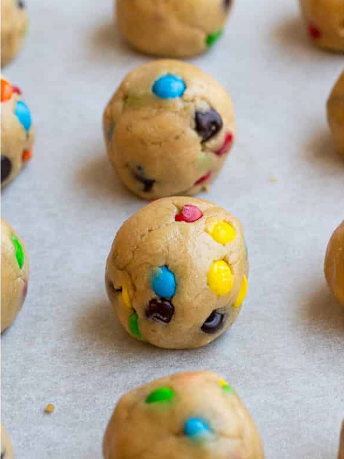 M and M peanut butter cookie dough scooped and rolled into balls on a parchment lined sheet.