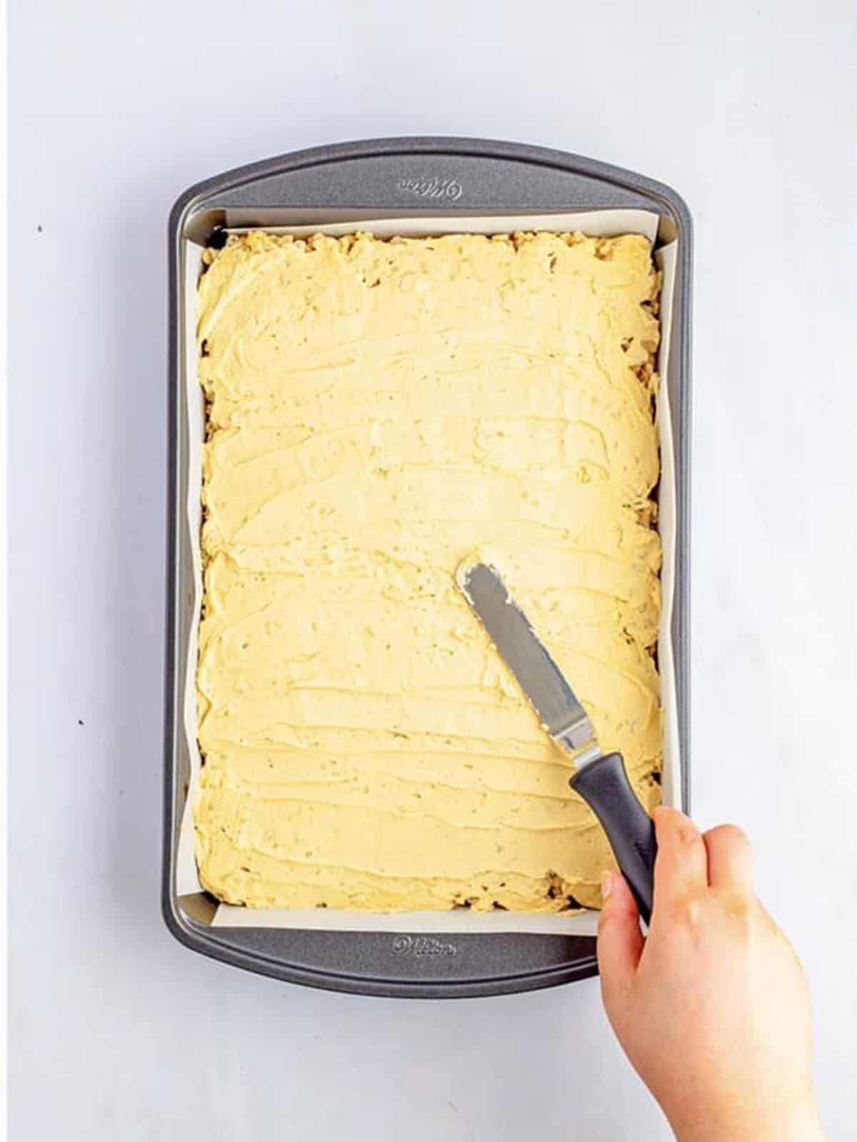 Peanut butter frosting spread over rice krispie treats in a pan.