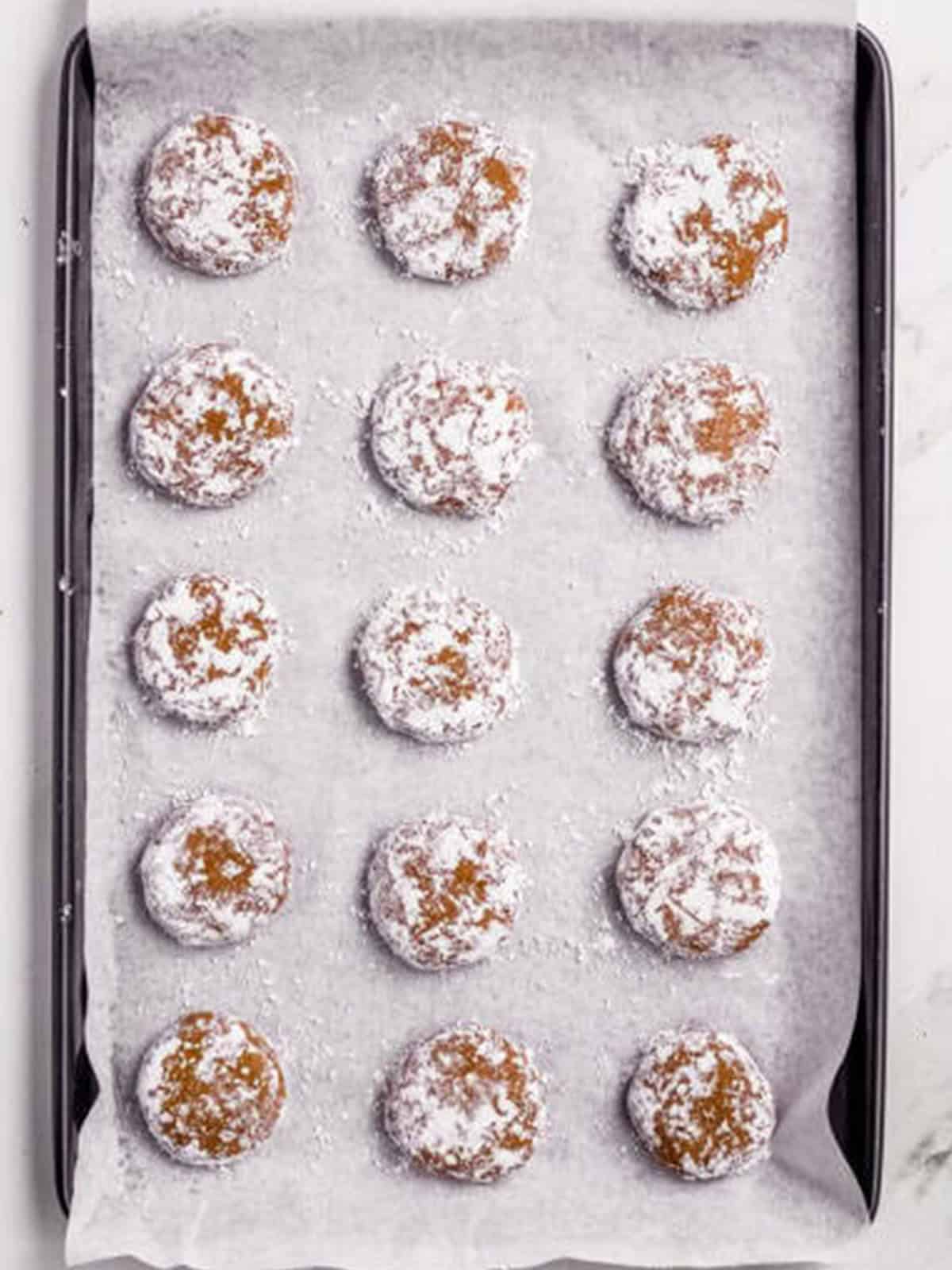 Powdered-sugar-coated molasses cookie dough balls on a baking sheet.
