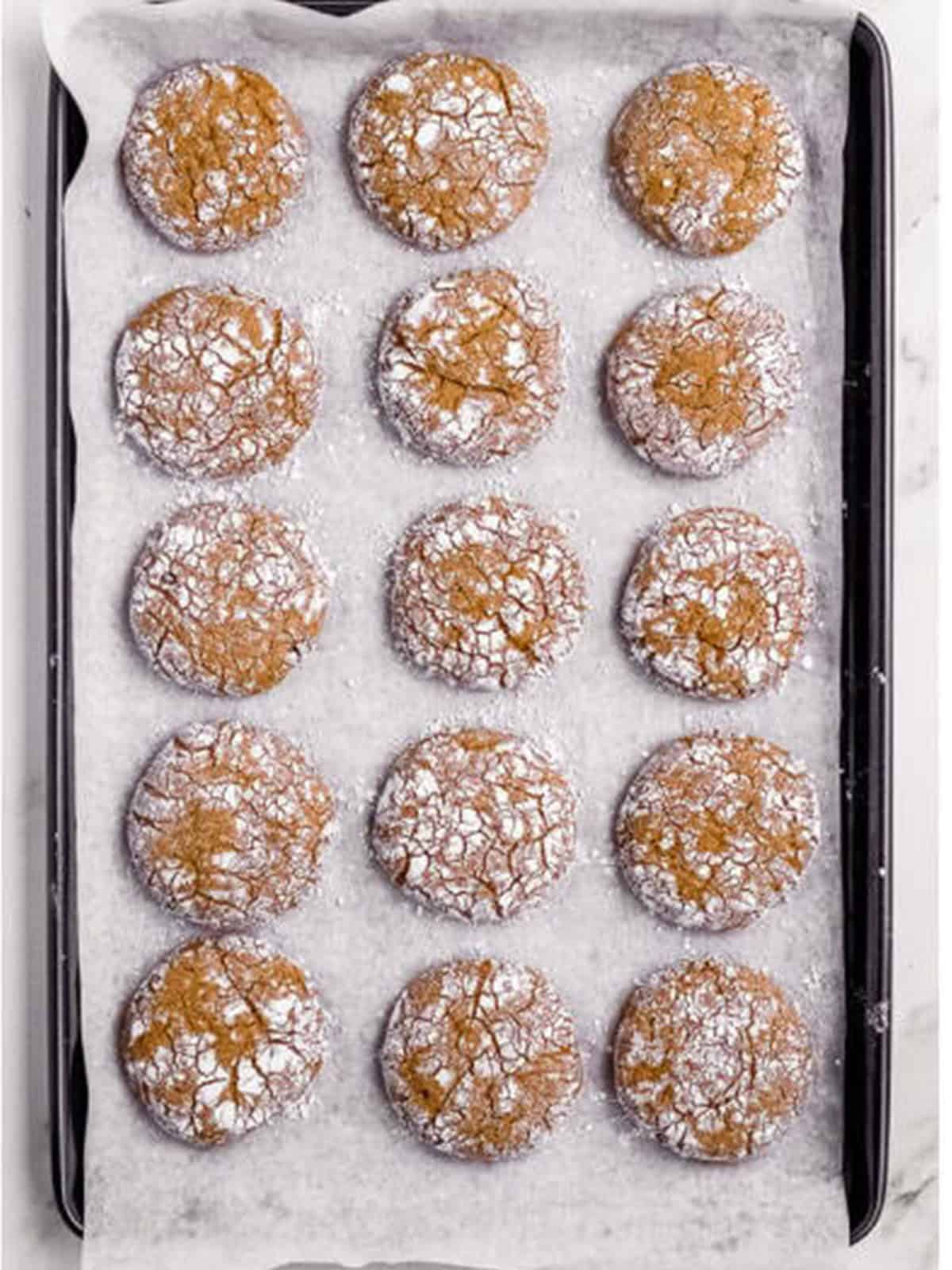 Baked crinkled molasses cookies on a parchment-lined baking sheet.