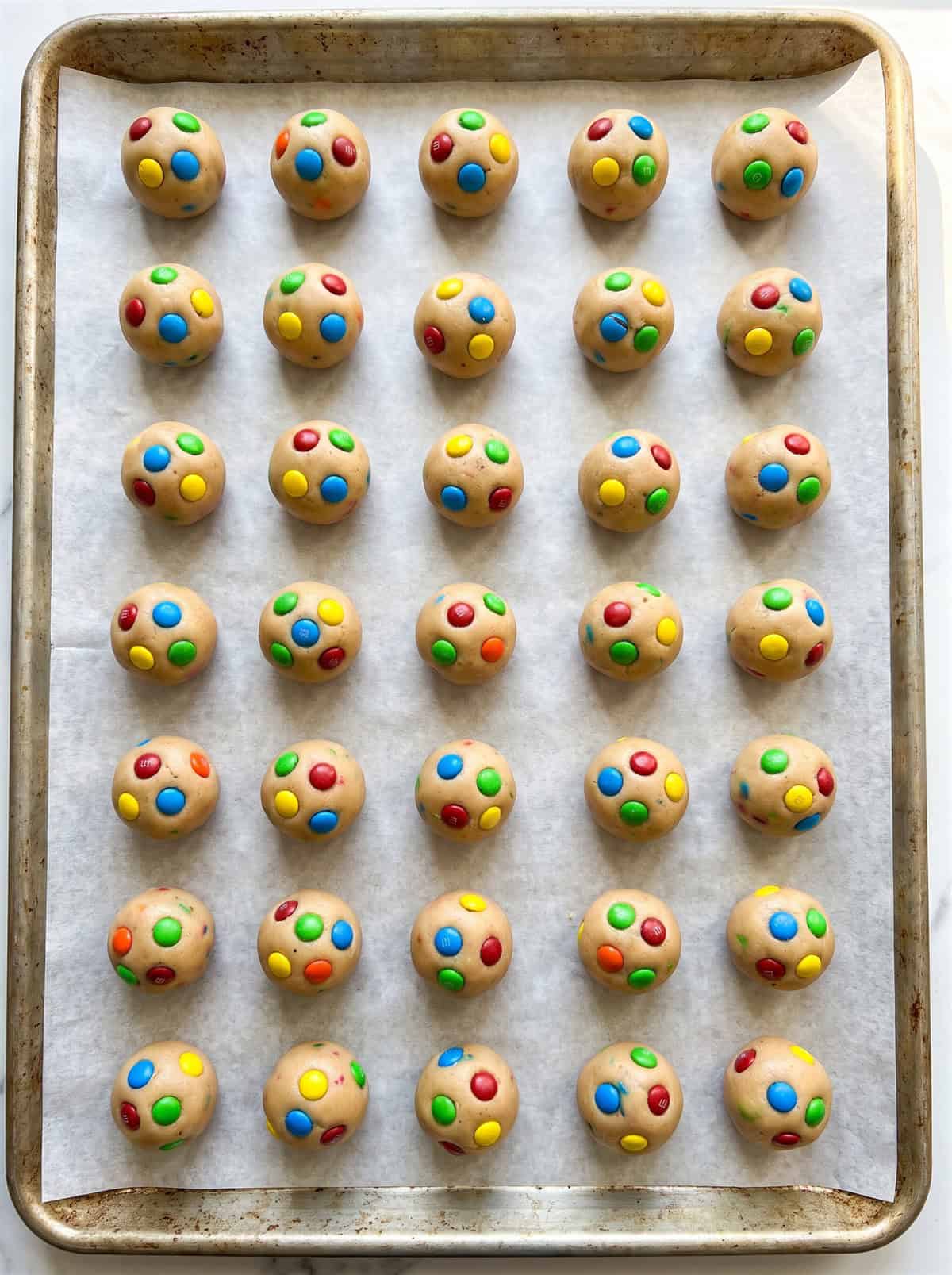 Small monster cookie dough balls on a parchment-lined baking sheet.