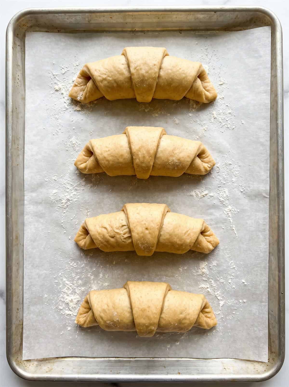 Four filled Monterey chicken crescent roll ups pinched closed on a parchment lined baking sheet before baking.
