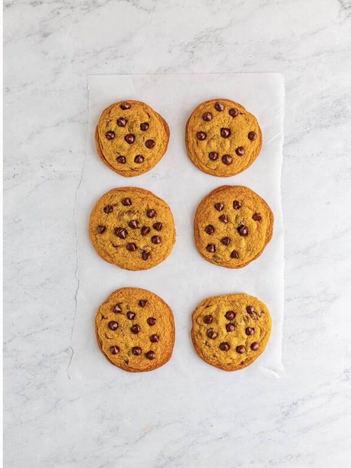 Baked copycat Mrs Fields chocolate chip cookies cooling on parchment paper.