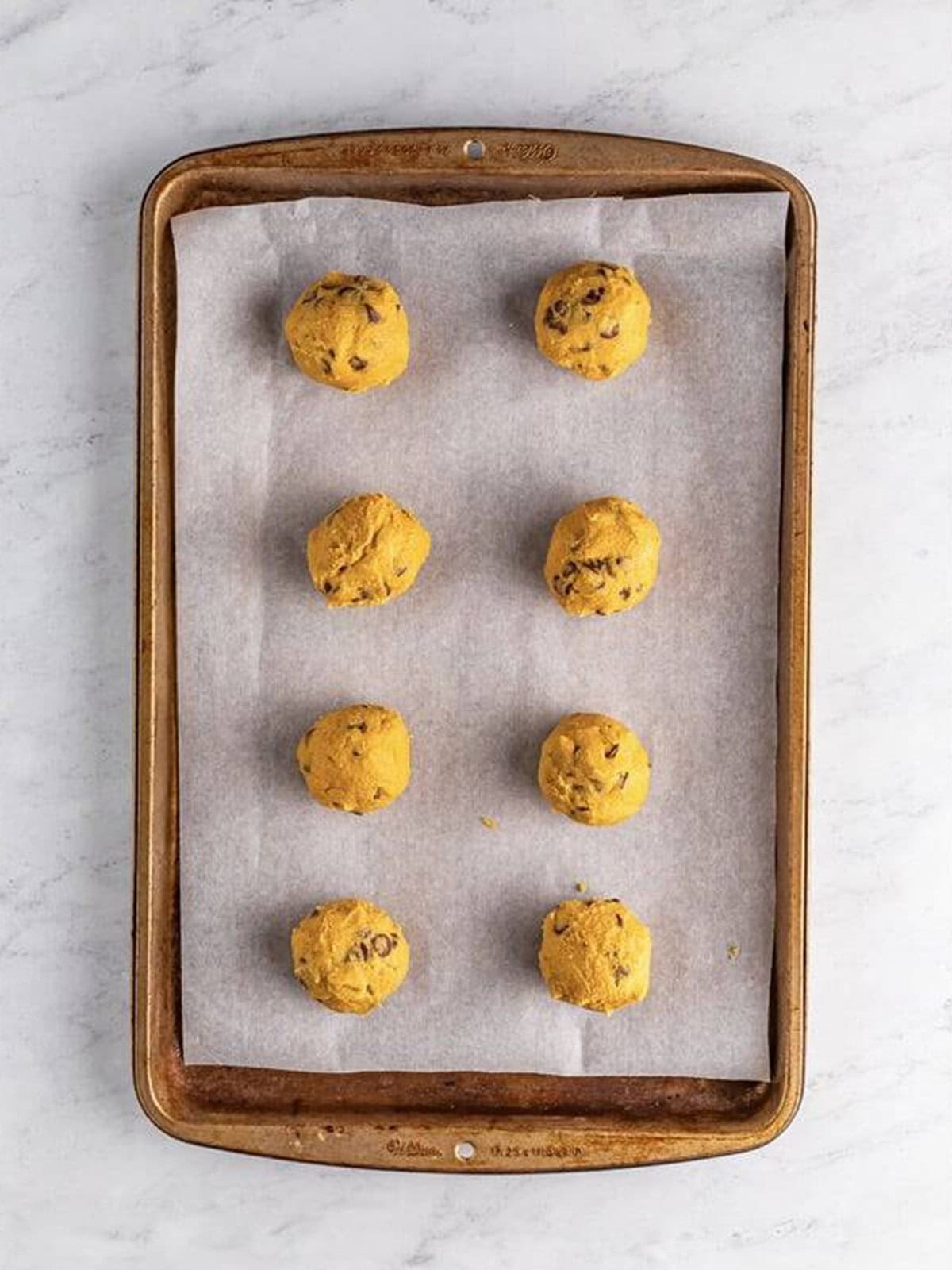 Mrs Fields cookie dough balls rolled and placed on a parchment lined sheet tray.