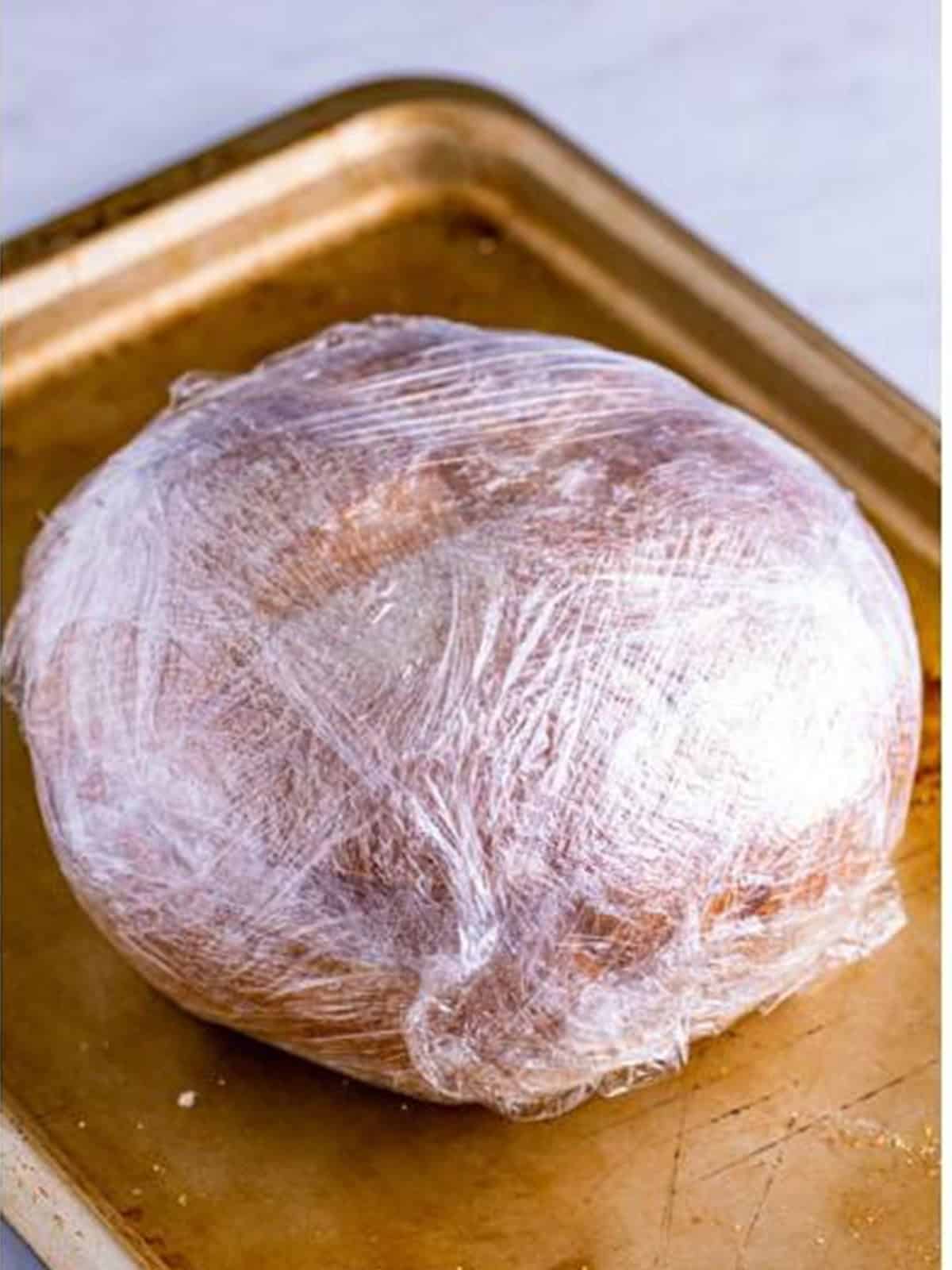The assembled muffuletta wrapped tightly in plastic wrap to press.