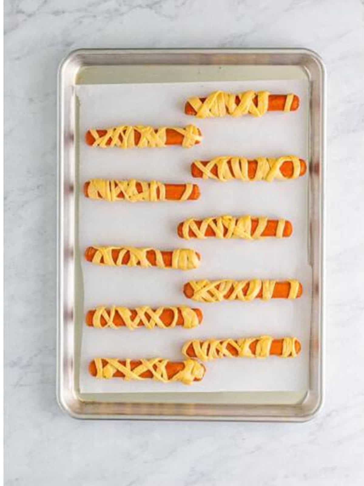 Wrapped mummy dogs arranged seam side down on a baking sheet.