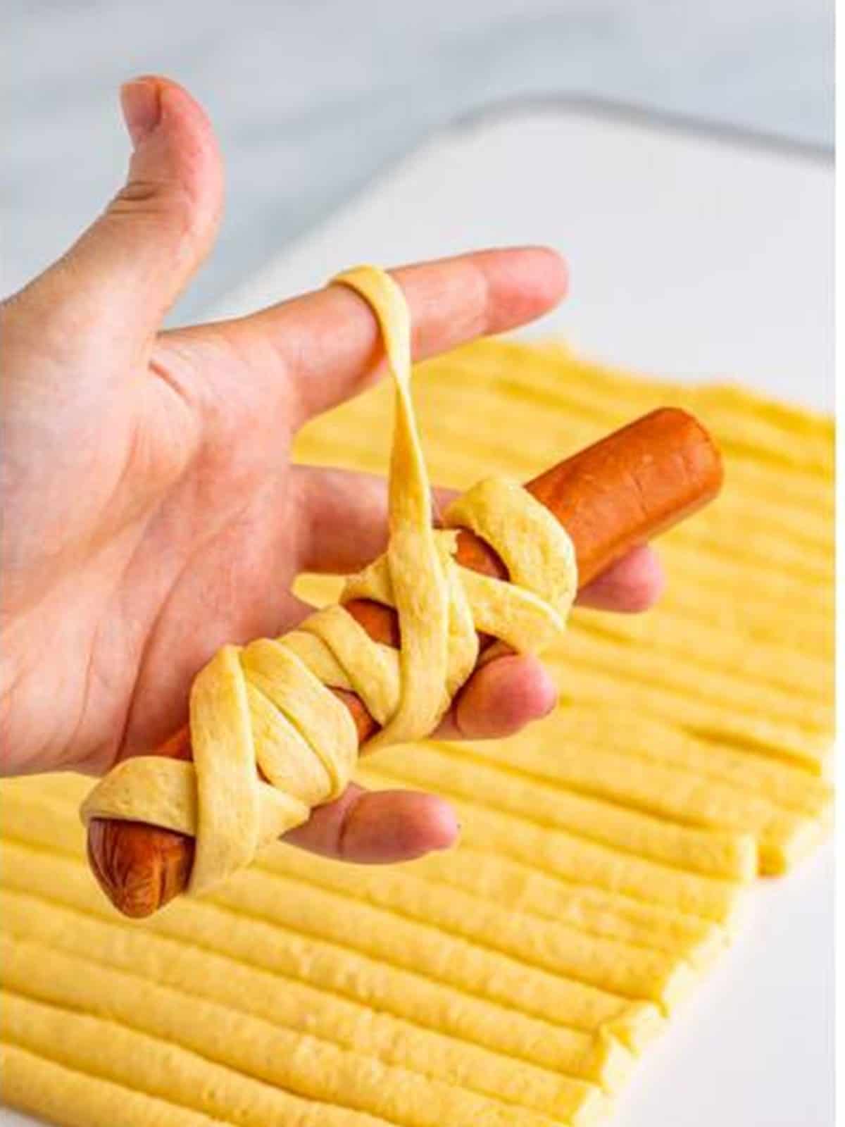 Wrapping a hot dog with strips of crescent dough to make a mummy dog.