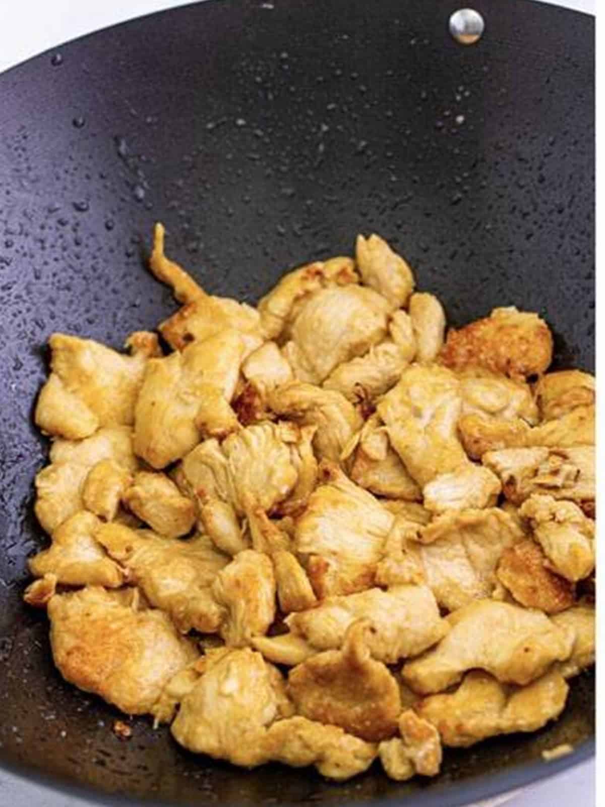 Sliced chicken searing golden brown in a single layer in a wok for mushroom chicken.