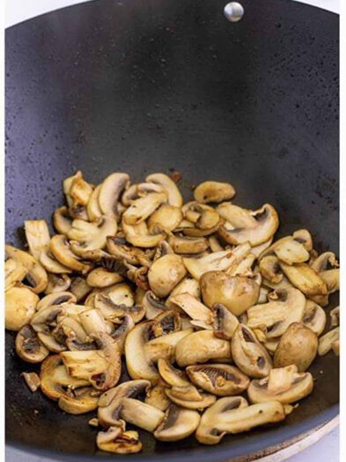 Sliced white mushrooms searing in a wok until softened.