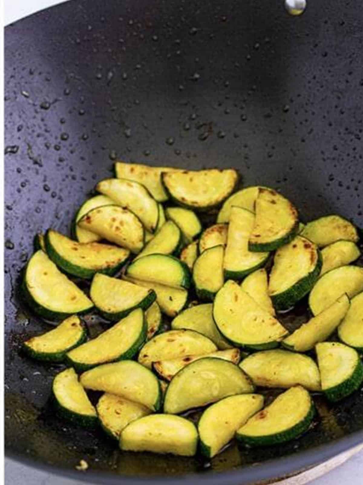 Half moon zucchini slices cooking until tender crisp in a wok.