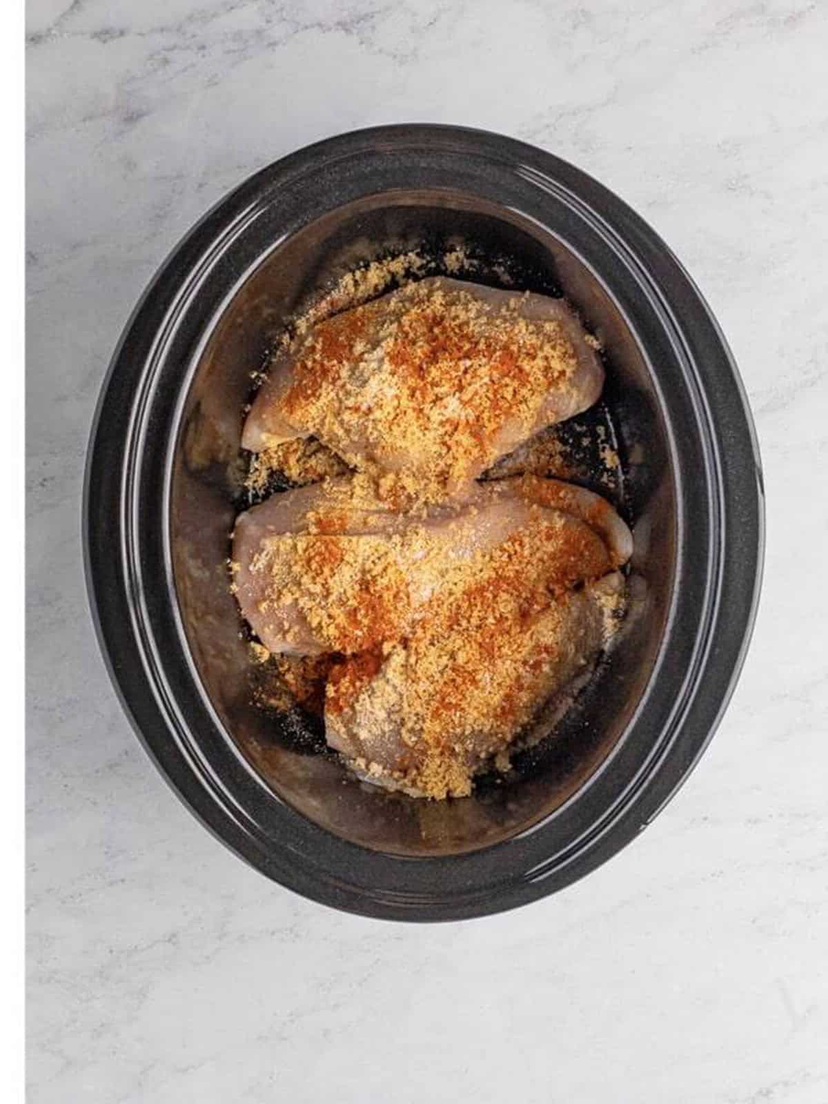Chicken breasts in a slow cooker sprinkled with brown sugar and spices.