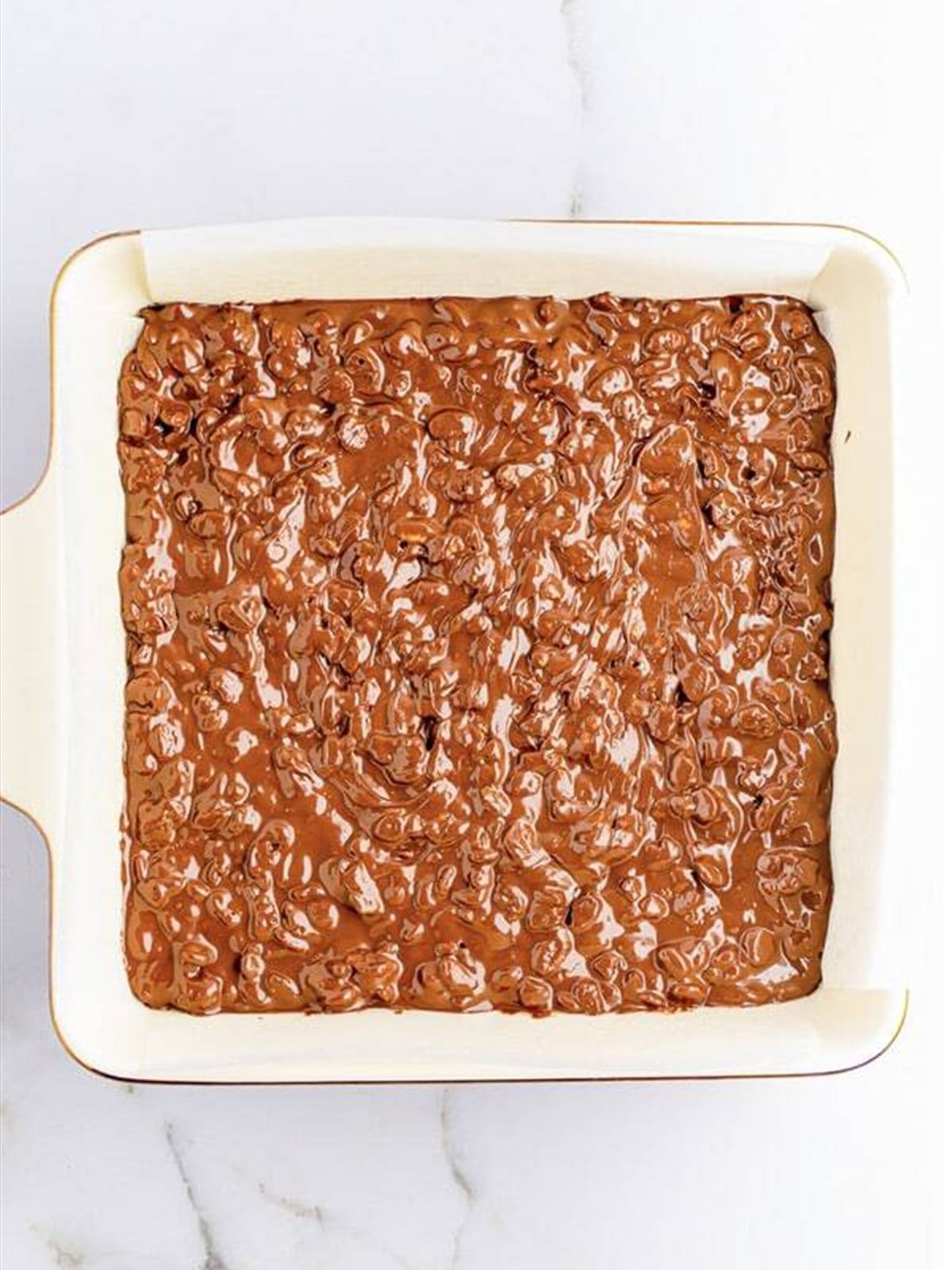 Chocolate cereal mixture spread in a parchment-lined pan.