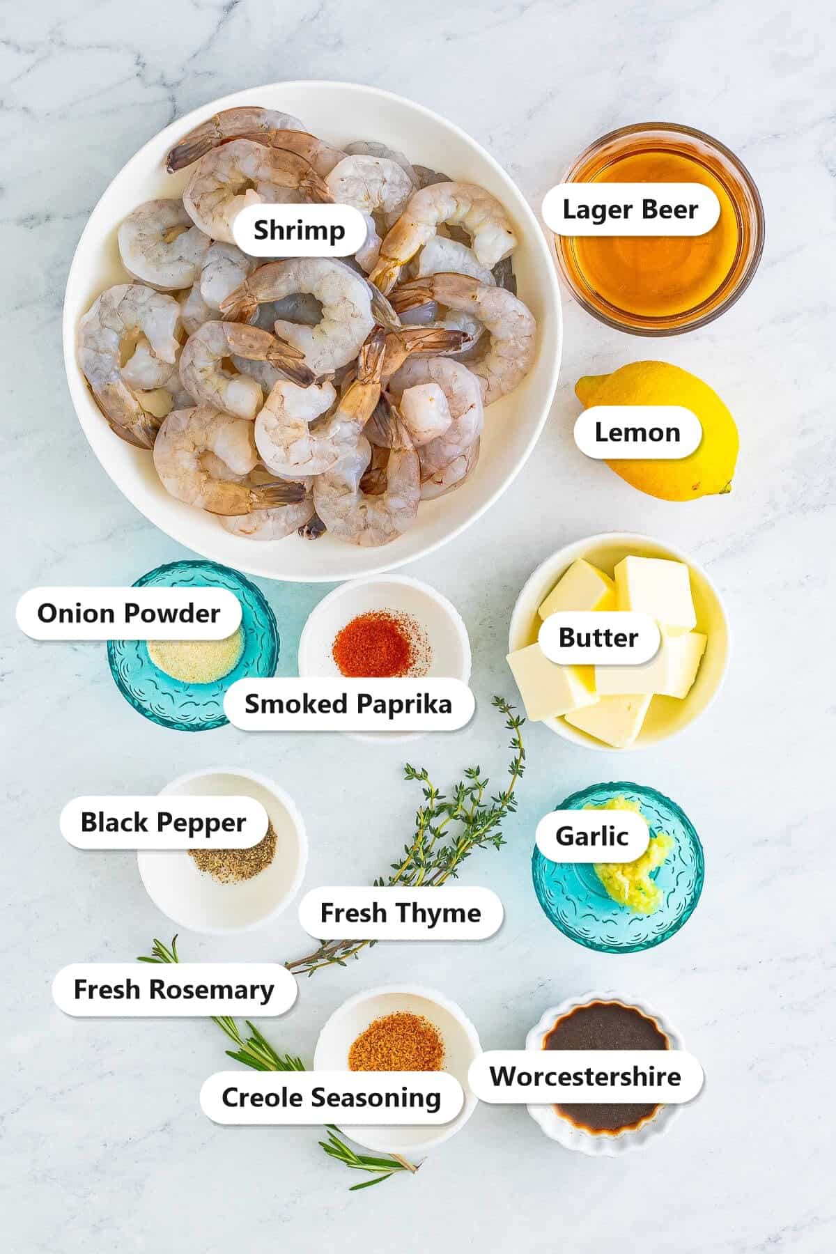 Ingredients to make New Orleans BBQ shrimp labeled including colossal shrimp, lager beer, lemon, butter, garlic, creole seasoning, smoked paprika, thyme, rosemary, onion powder, black pepper, and Worcestershire sauce.