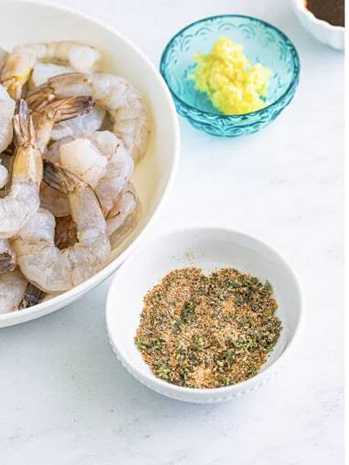 Creole seasoning blend mixed in a bowl next to raw shrimp for New Orleans BBQ shrimp.
