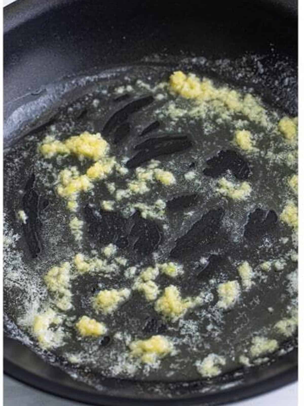 Minced garlic sauteing in melted butter in a skillet.