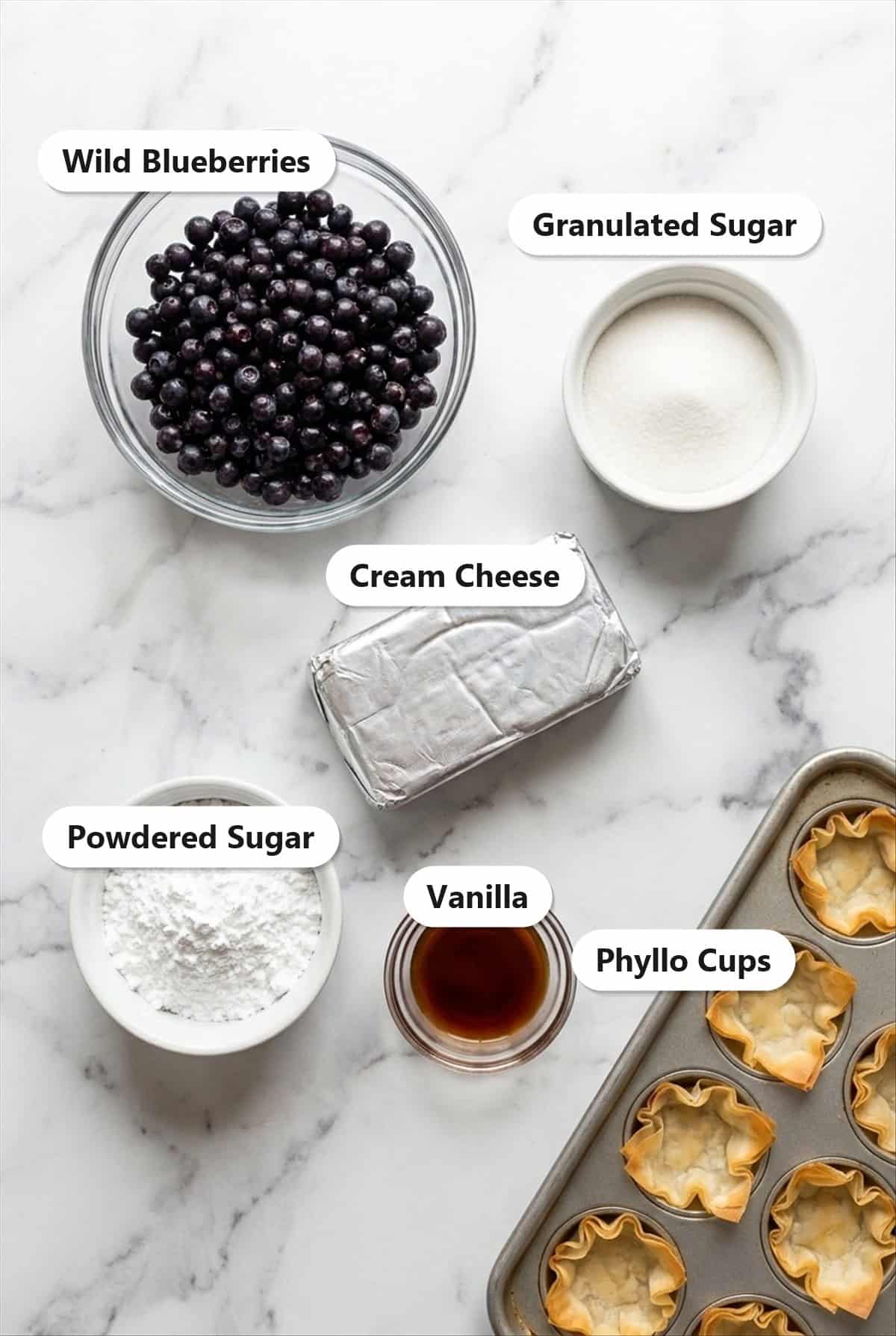 Labeled ingredients for wild blueberry no bake cheesecake bites including wild blueberries, cream cheese, powdered sugar, granulated sugar, vanilla, and mini phyllo cups.