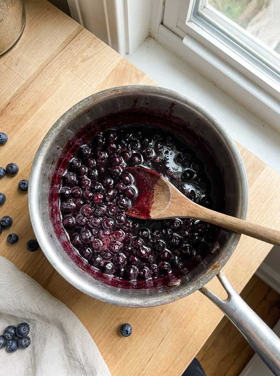 Wild blueberries simmering into a thick glossy blueberry sauce in a saucepan.