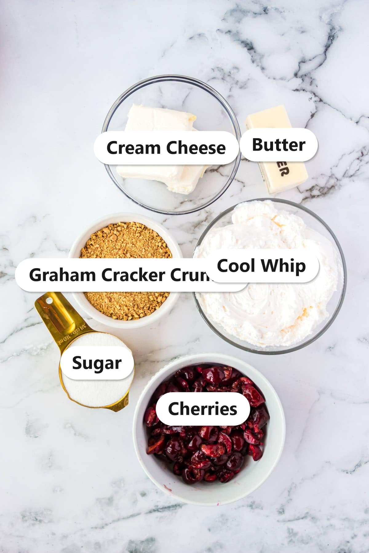 Labeled ingredients for no bake cherry cheesecake including cream cheese, graham cracker crumbs, butter, cool whip, sugar, and fresh cherries.