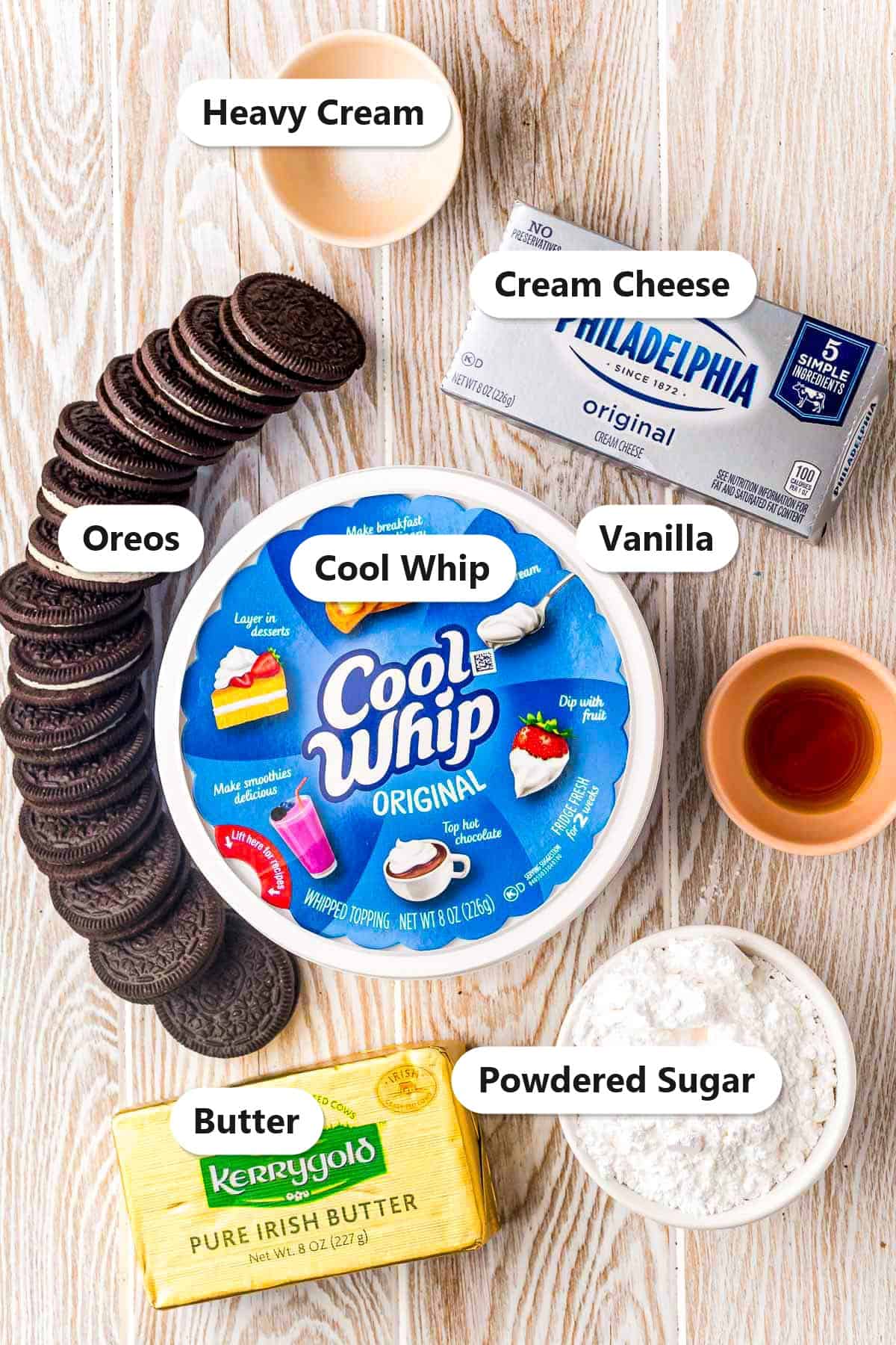 Labeled ingredients for no bake Oreo cheesecake including Oreos, cream cheese, Cool Whip, powdered sugar, butter, and vanilla.