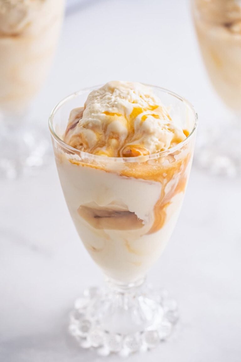 A parfait glass of no churn caramel ice cream drizzled with caramel sauce.