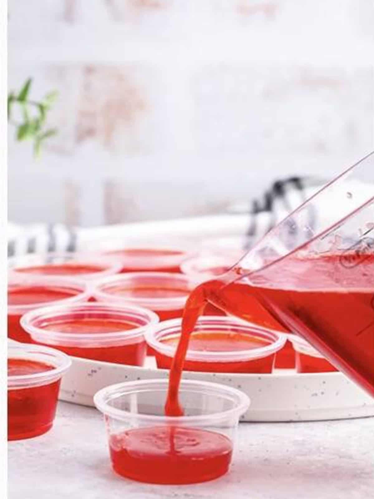 Pouring the jello mixture into small plastic shot cups.