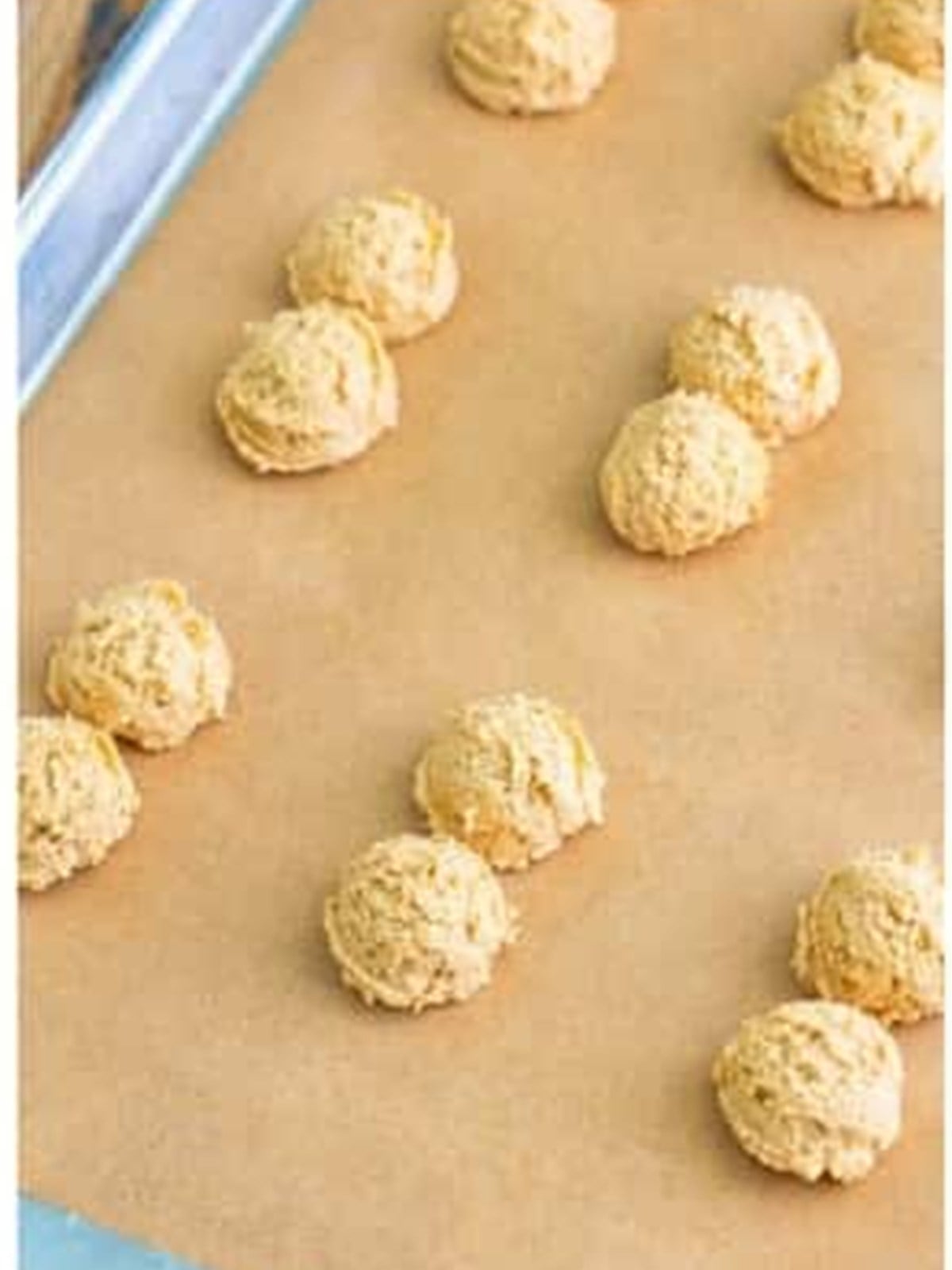 Pairs of peanut butter cookie dough dollops on a parchment-lined tray.