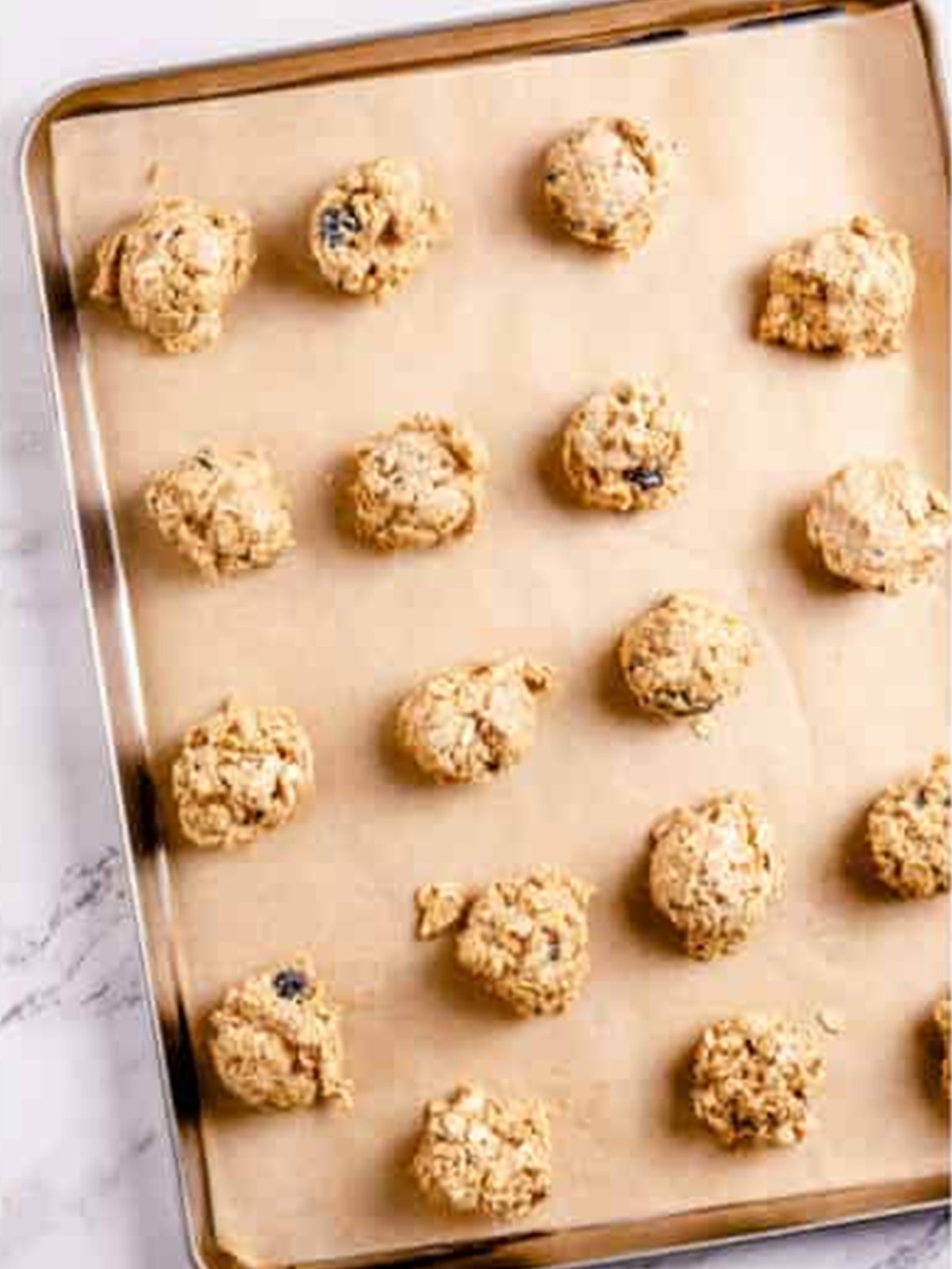 Oatmeal blueberry cookie dough scooped into mounds on a parchment lined baking sheet.