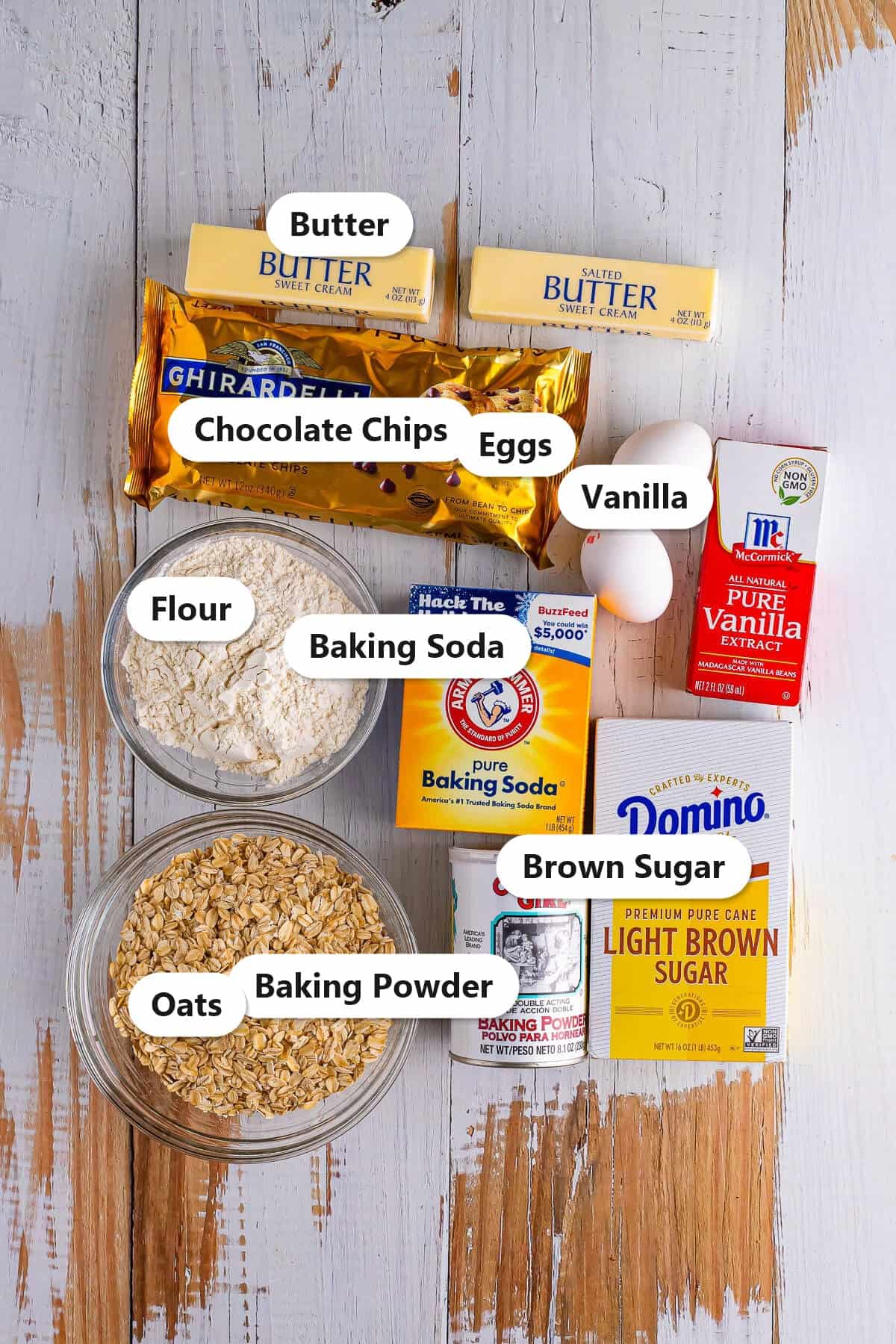 Labeled ingredients to make oatmeal chocolate chip cookie bars including butter, chocolate chips, eggs, vanilla, flour, oats, brown sugar, and leaveners.