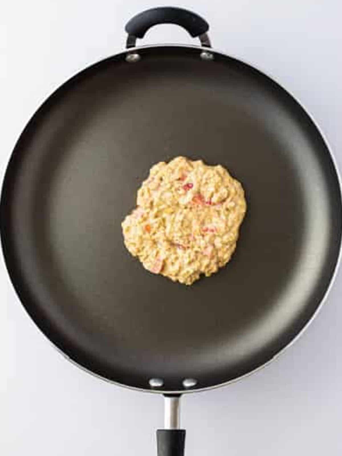Oatmeal pancake batter spread into a circle and cooking in a skillet.