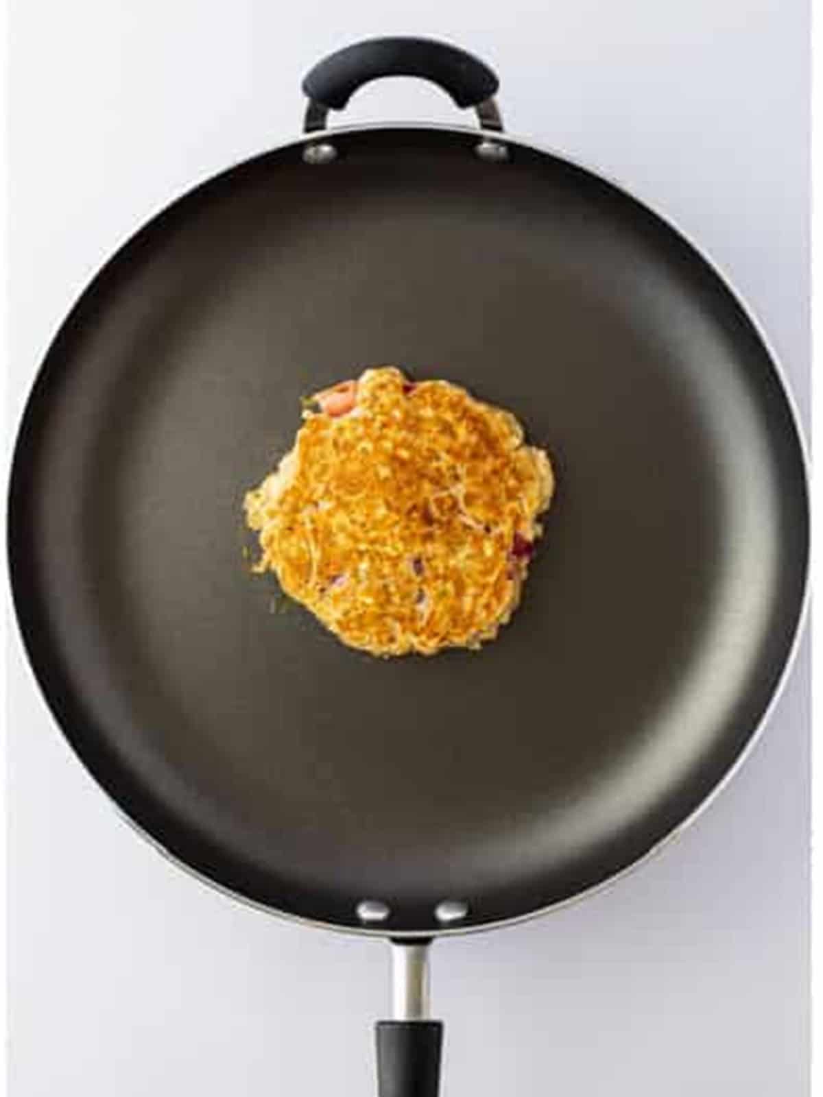 A golden brown strawberry oatmeal pancake flipped in the skillet.
