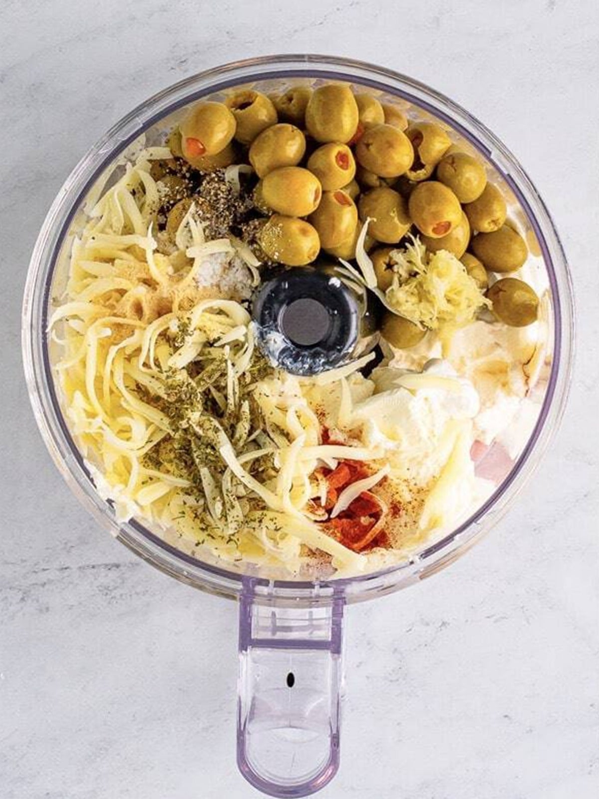 Olives, cream cheese, and seasonings in a food processor for olive dip.